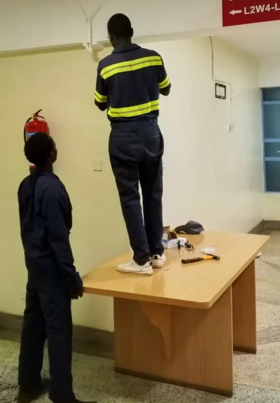 Two CLAUDNET technicians installing a WiFi access point in a building corridor