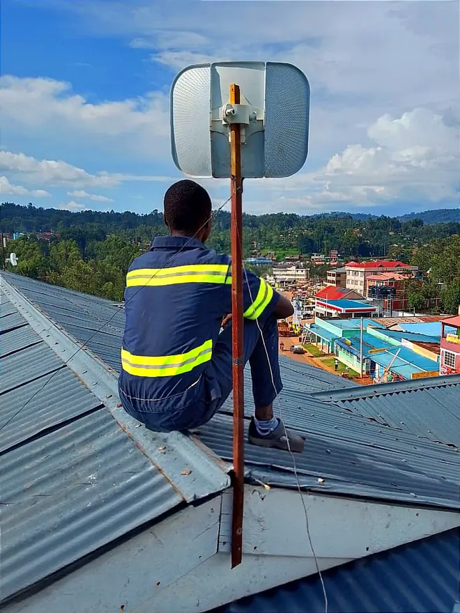 CLAUDNET technician on a rooftop beside a wireless antenna, overlooking Kisii Town